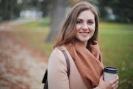 Portrait of a smiling woman holding a coffee cup in a serene autumn park setting.